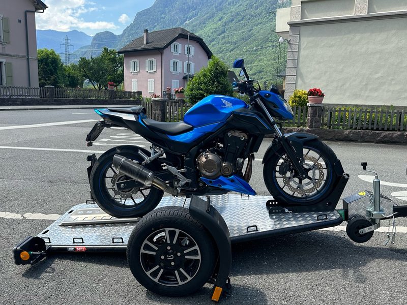 Moto naked bleue arrimée sur la remorque Lorries MT-1, village valaisan et montagnes en arrière-plan